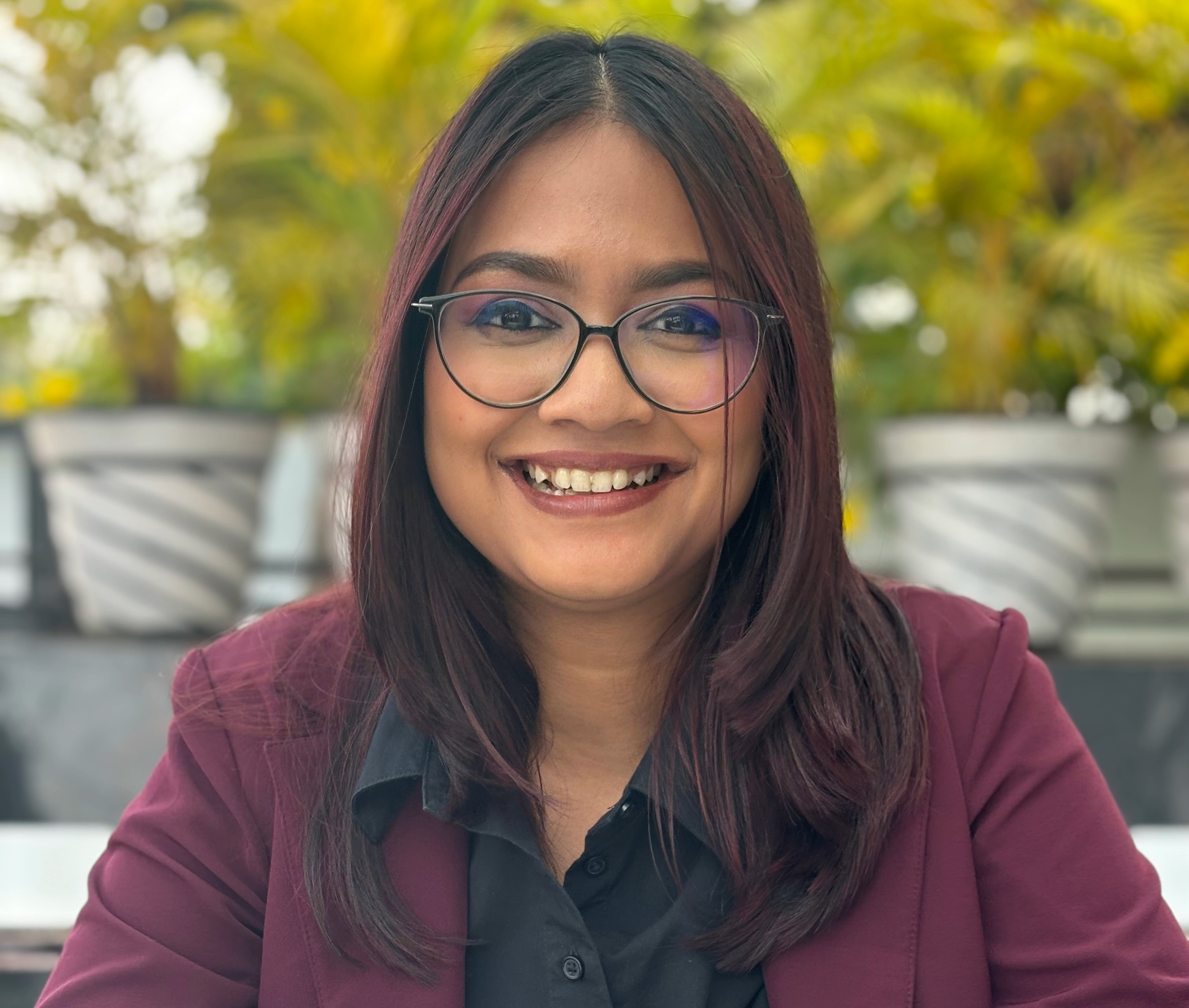 Bhumika Sheth smiling in a red plaid shirt and tortoise shell glasses